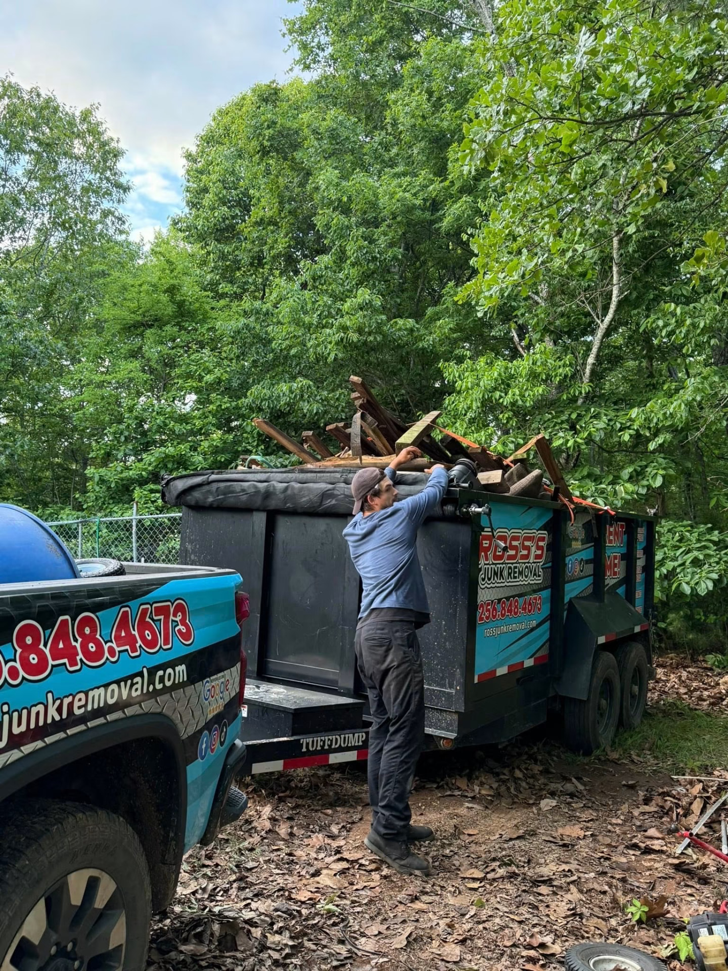 Ross's Junk Removal crew strapping down a dump trailer loaded with lumber and debris